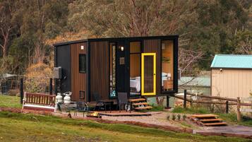 A cabin with a deck, outdoor seating, and a visible interior with a bed.