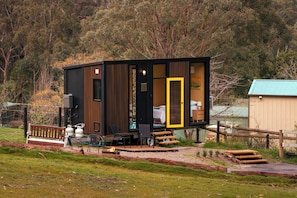 A cabin with a deck, outdoor seating, and a visible interior with a bed.