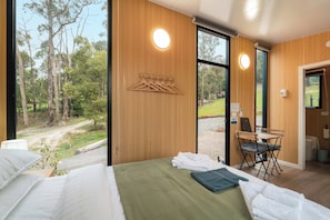 A bedroom with a bed, a desk, and a view of the outdoors.