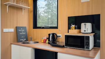 A compact kitchenette with a microwave, kettle, and a small coffee maker. There is a window above the sink, and a welcome sign is visible on the wall.
