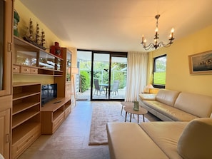 Ein Wohnzimmer mit einer Couch, Fernseher, Holzregalen und einem Balkon mit Gartenmöbeln.