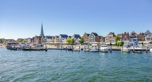 A waterfront town with historic buildings, a church spire, and boats docked along the pier. - Hafenliebe Travemünde - "Hafenliebe" Vacation Rental – A Beachfront Vacation in (Lübeck)