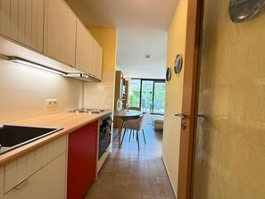 Eine moderne Küche mit einer roten Kochinsel, einem Essbereich mit Tisch und Stühlen sowie ein Blick durch eine Glastür in einen Außenbereich.