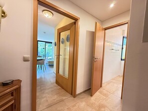 Un couloir avec une porte en bois qui donne sur une salle à manger, où se trouvent une table et des chaises.
