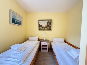 Une chambre avec deux lits simples, une table de chevet avec une lampe et deux tableaux au mur.
