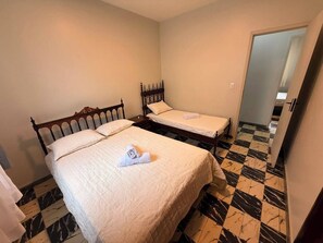 Una habitación con dos camas, piso a cuadros y una puerta que da a otra estancia.