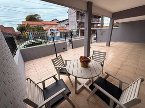 Ein Balkon mit rundem Tisch, vier Stühlen, einer Blumenvase und Blick auf Gebäude sowie einen Zaun im Hintergrund.
