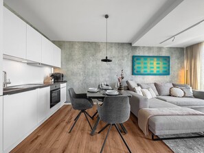 Une cuisine moderne avec des meubles blancs, un coin repas avec une table dressée pour quatre personnes, et un canapé gris dans l’espace salon.