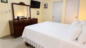 A bedroom with a bed, dresser, ceiling fan, TV, and two doors. - A beautiful, comfortable, and safe home for the whole family (Santo Domingo Este)