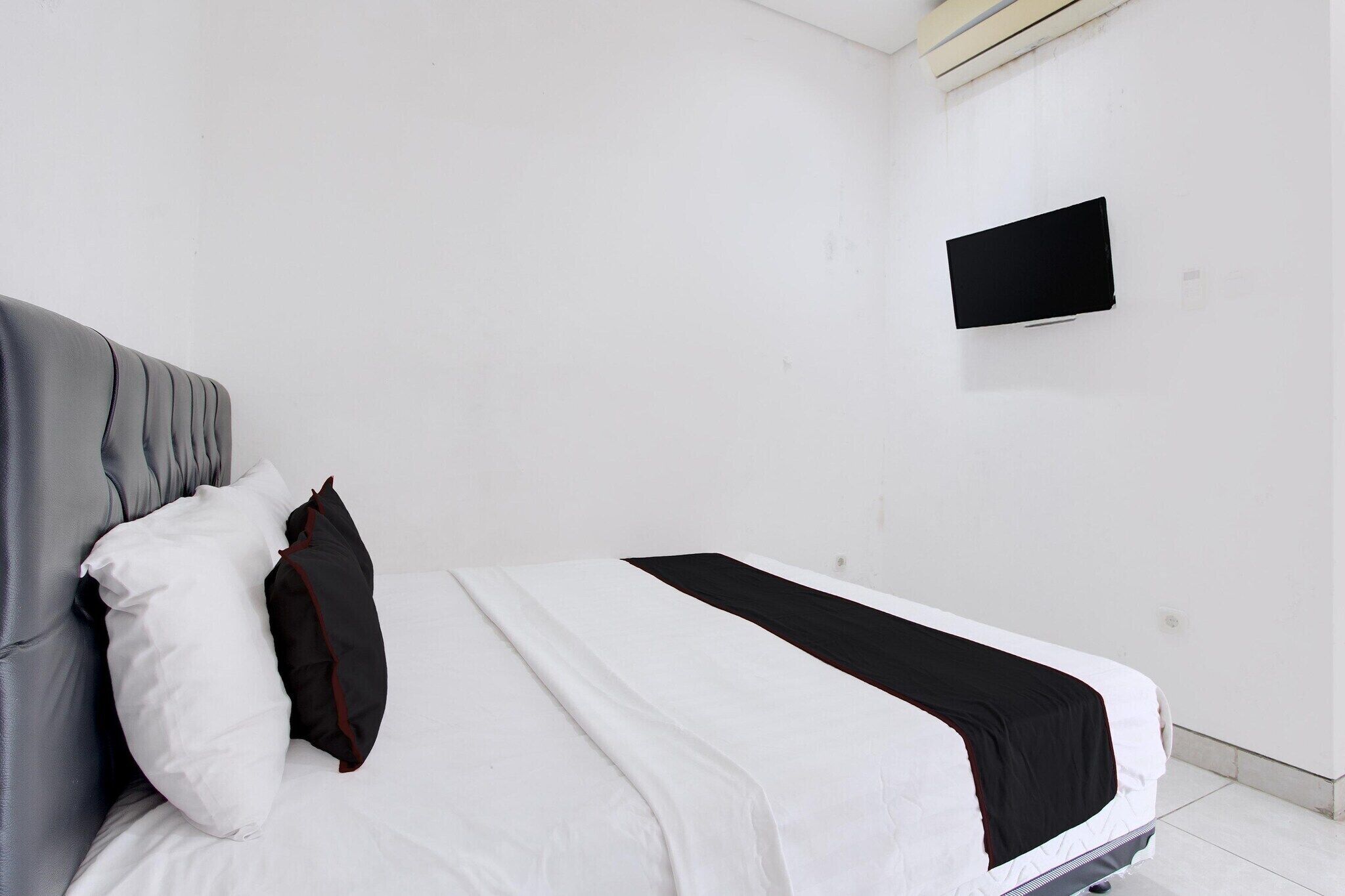 Ein schlichtes, sauberes Hotelzimmer mit einem Bett, einem wandmontierten Flachbildfernseher und einer schlichten weißen Wand.