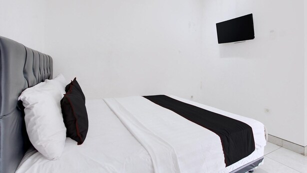 Una camera d'albergo semplice e pulita, con un letto, una TV a schermo piatto montata a parete e una parete bianca.
