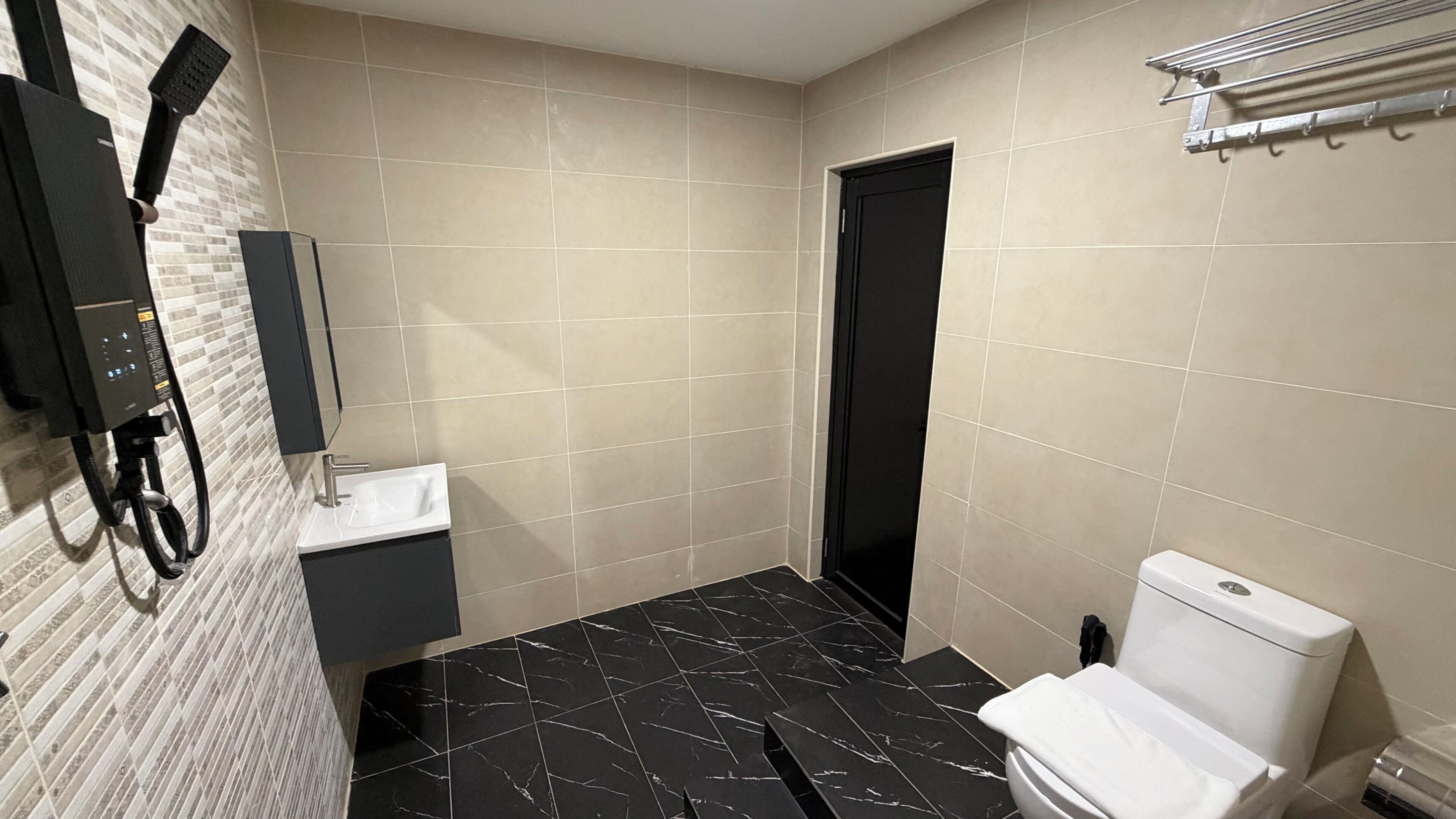 Un baño con piso de mármol negro, lavamanos blanco, inodoro negro y un perchero.