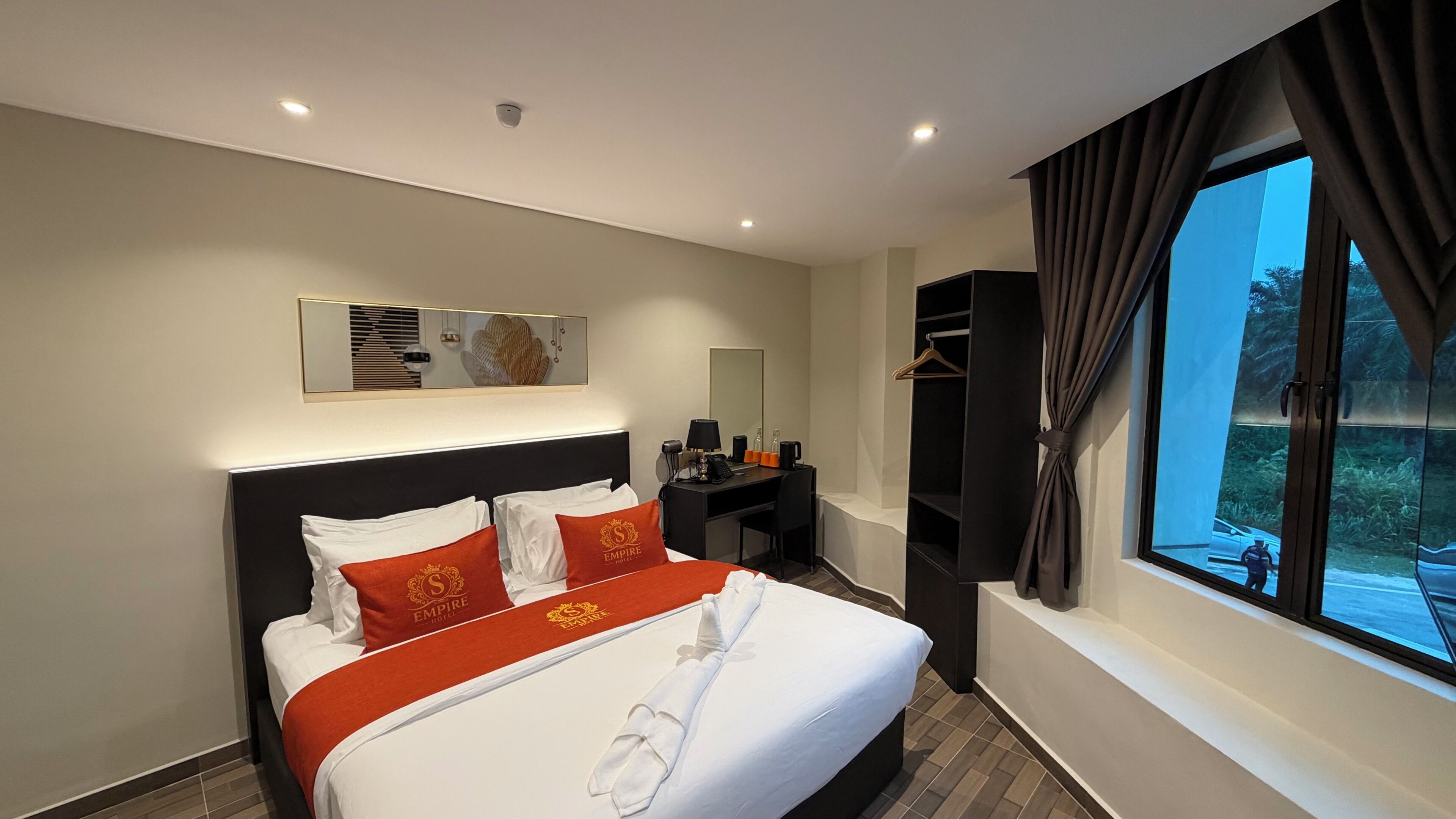 Habitación de hotel con cama, escritorio, silla, espejo y ventana con cortinas.
