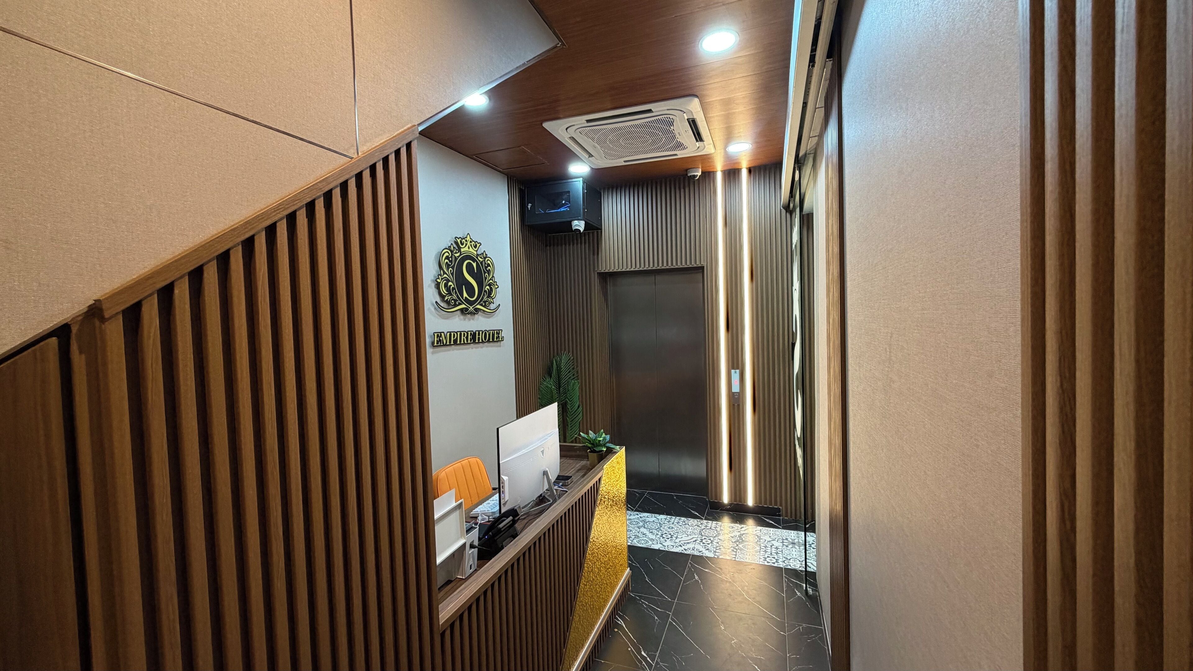 A reception area with a wooden slat wall, a reception desk, a wall-mounted television, and an elevator.