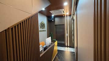 A reception area with a wooden slat wall, a reception desk, a wall-mounted television, and an elevator.