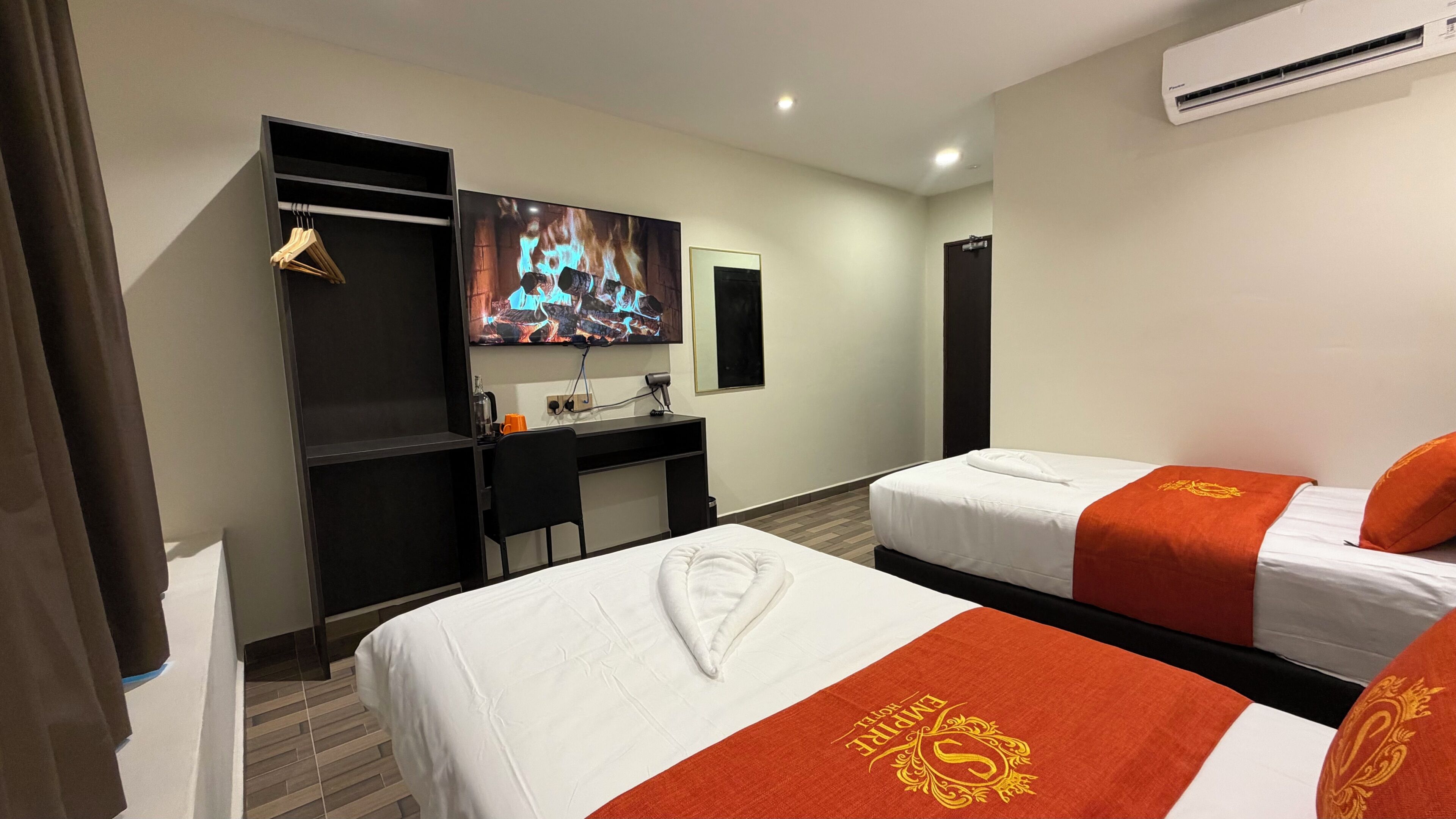 Quarto de hotel com duas camas, uma escrivaninha, televisão e ar condicionado.