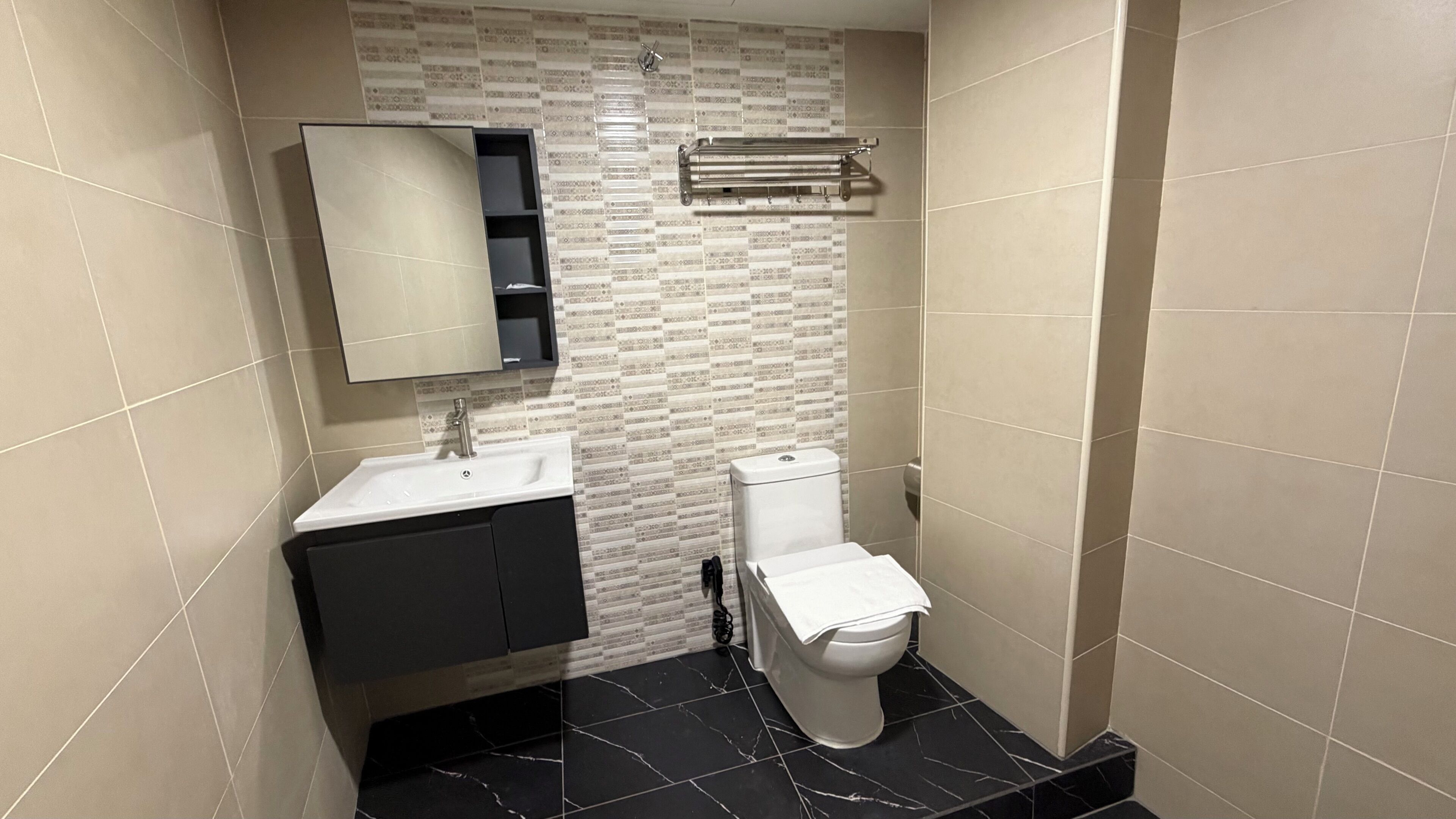 Un baño con lavamanos blanco, un espejo, un inodoro y un perchero para toallas.