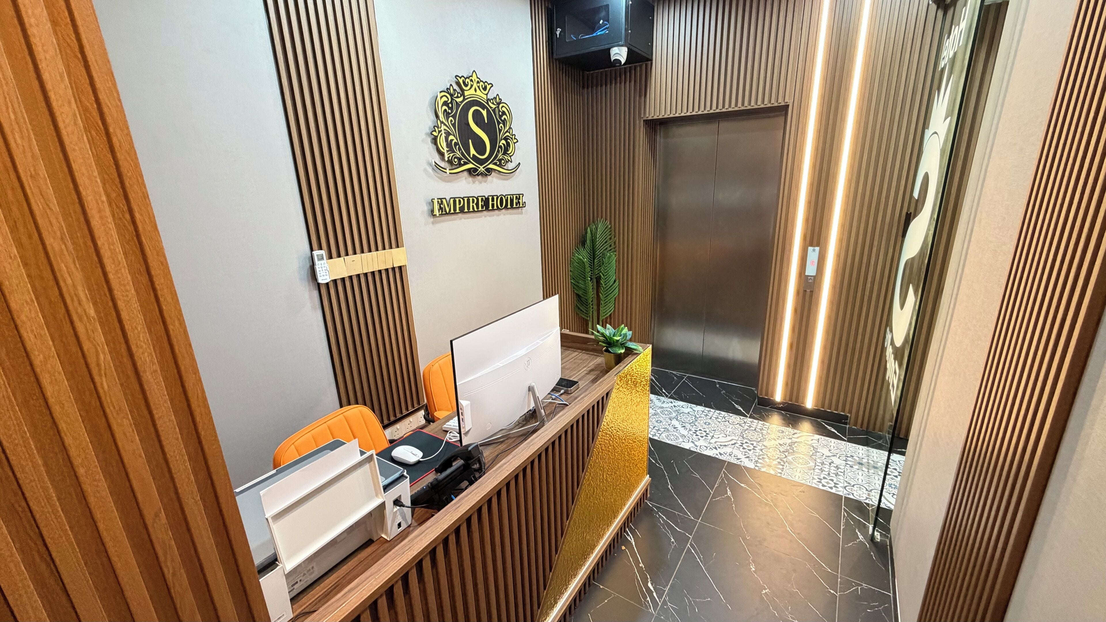 Mostrador de recepción de hotel con computadora, teléfono y una planta.