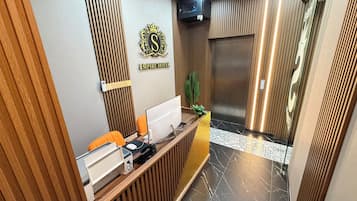 Mostrador de recepción de hotel con computadora, teléfono y una planta.