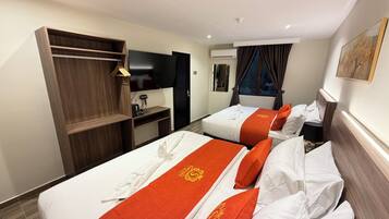 A hotel room with two beds, a TV, a wardrobe, and a window with curtains.