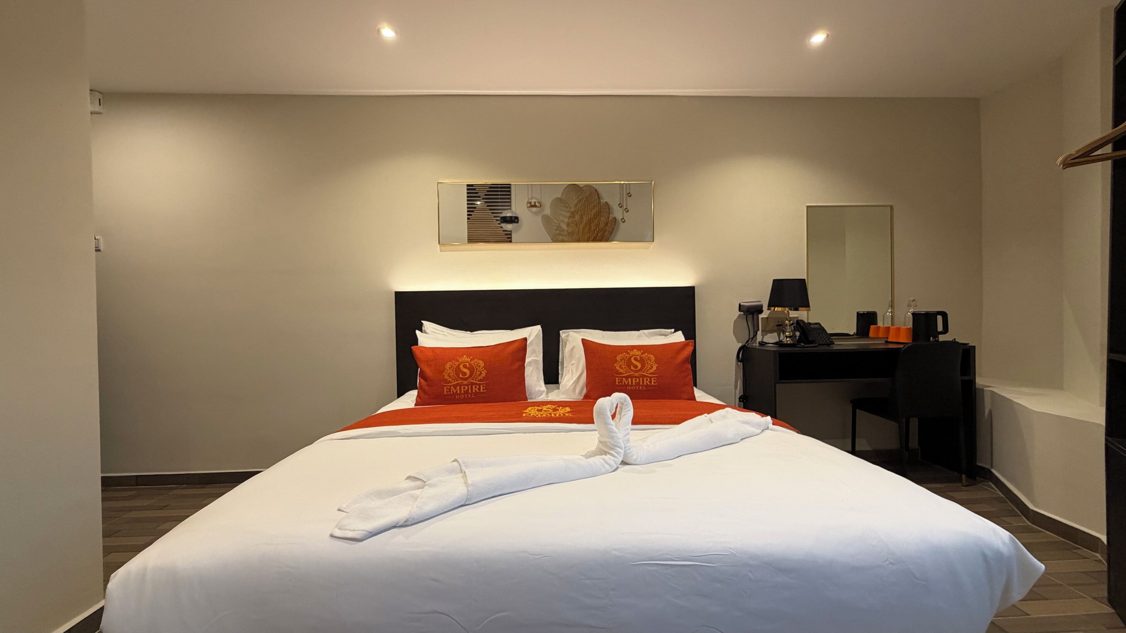 Habitación de hotel con cama, escritorio, silla, espejo y una obra de arte en la pared.