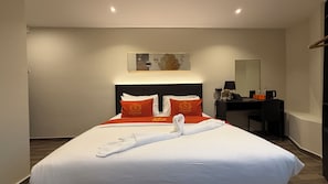 A hotel room with a bed, a desk, a chair, a mirror, and a wall-mounted artwork.