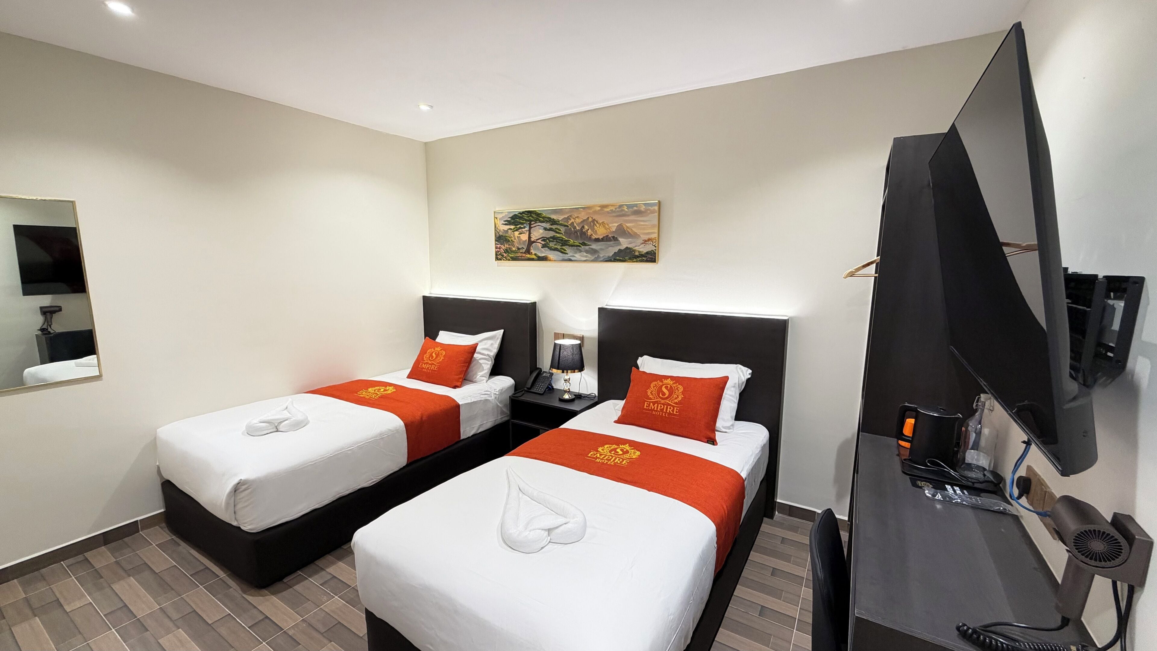 A hotel room with two beds, a flat-screen TV, a desk with a computer, and a painting on the wall.