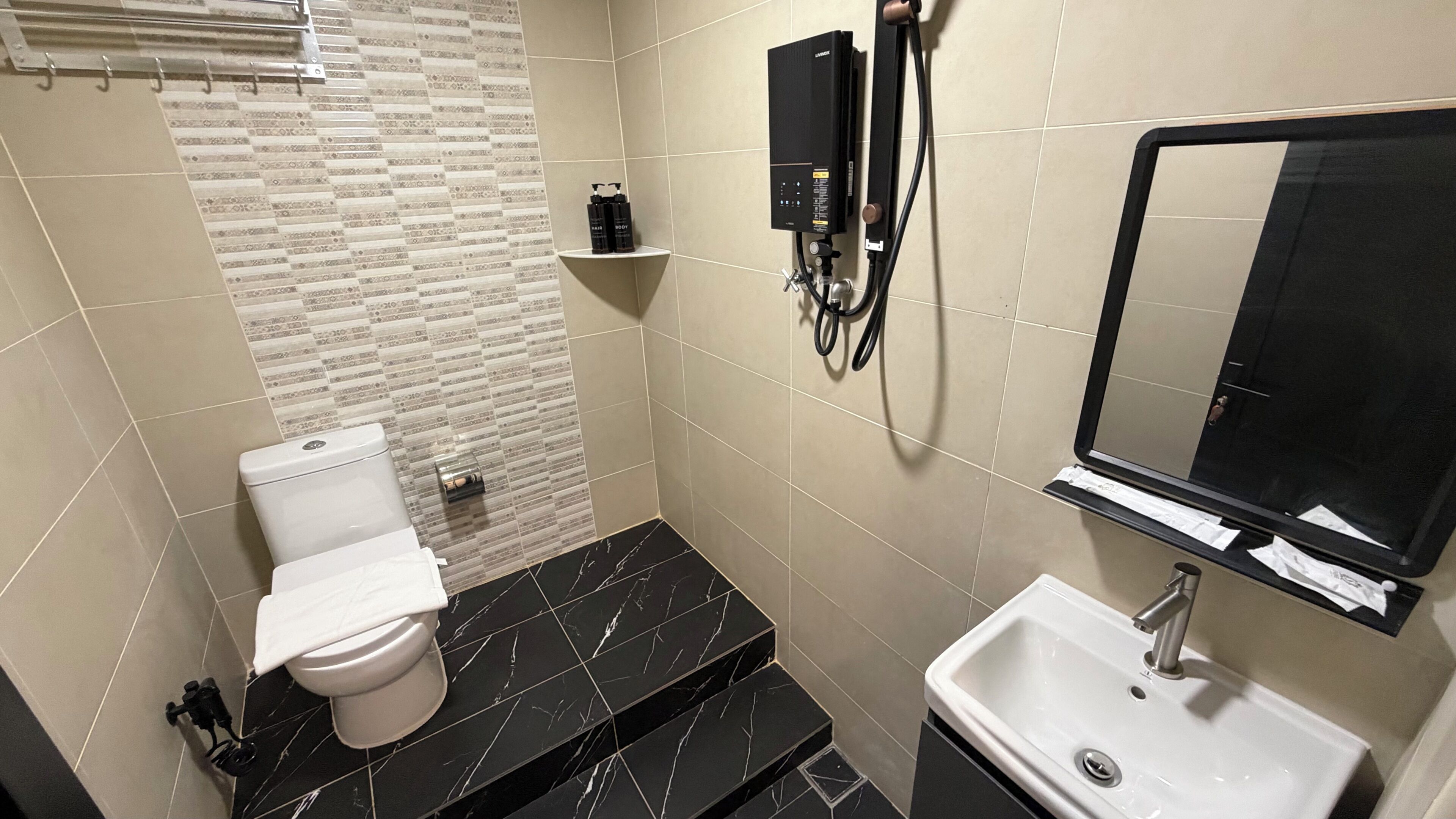 A bathroom with a toilet, a sink, a mirror, and a shower unit.