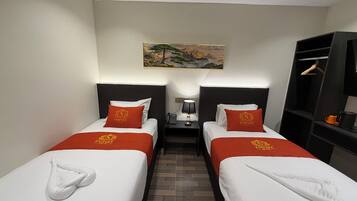 Habitación de hotel con dos camas individuales, una mesita de noche con lámpara, un cuadro en la pared y un armario.