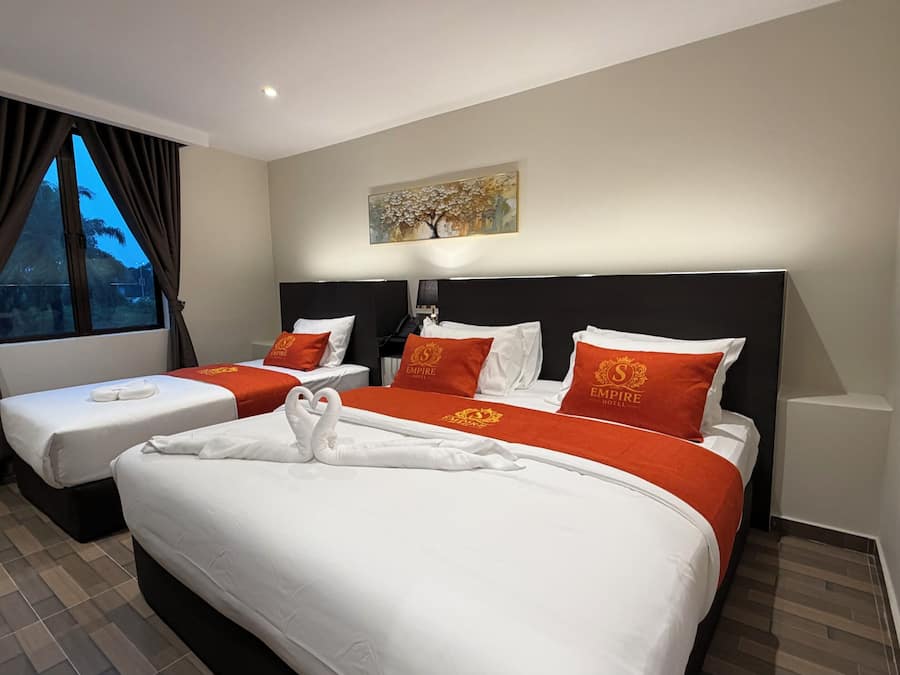 A hotel room with two beds, a painting on the wall, and an air conditioning unit.