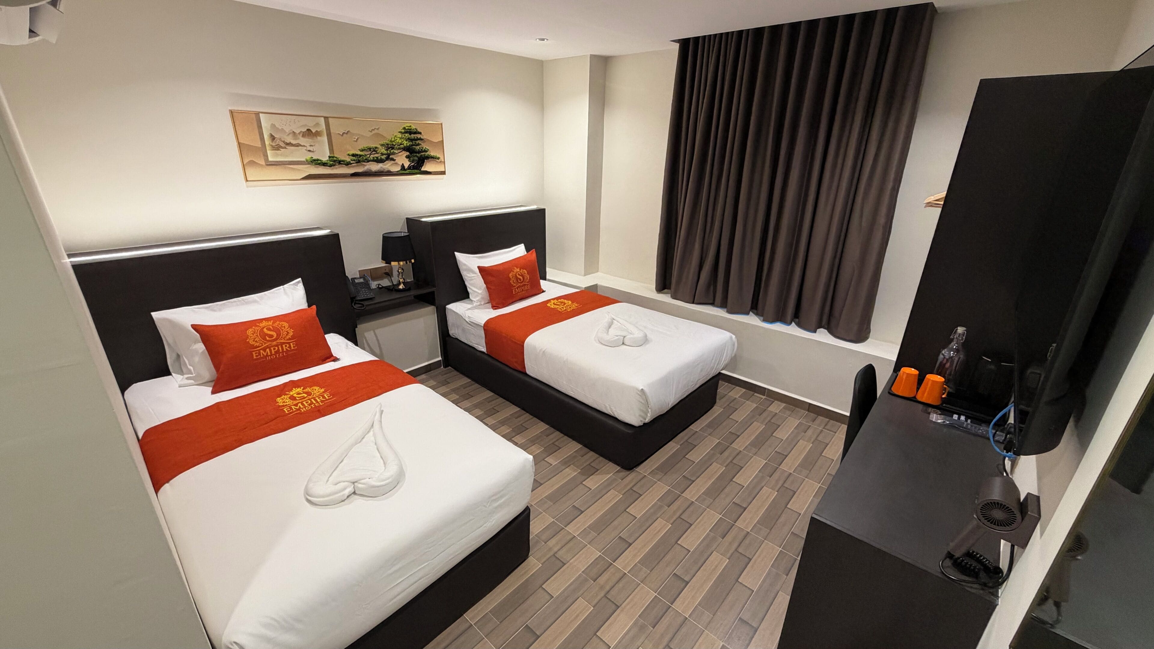 A hotel room with two beds, a desk, a TV, and a painting on the wall.