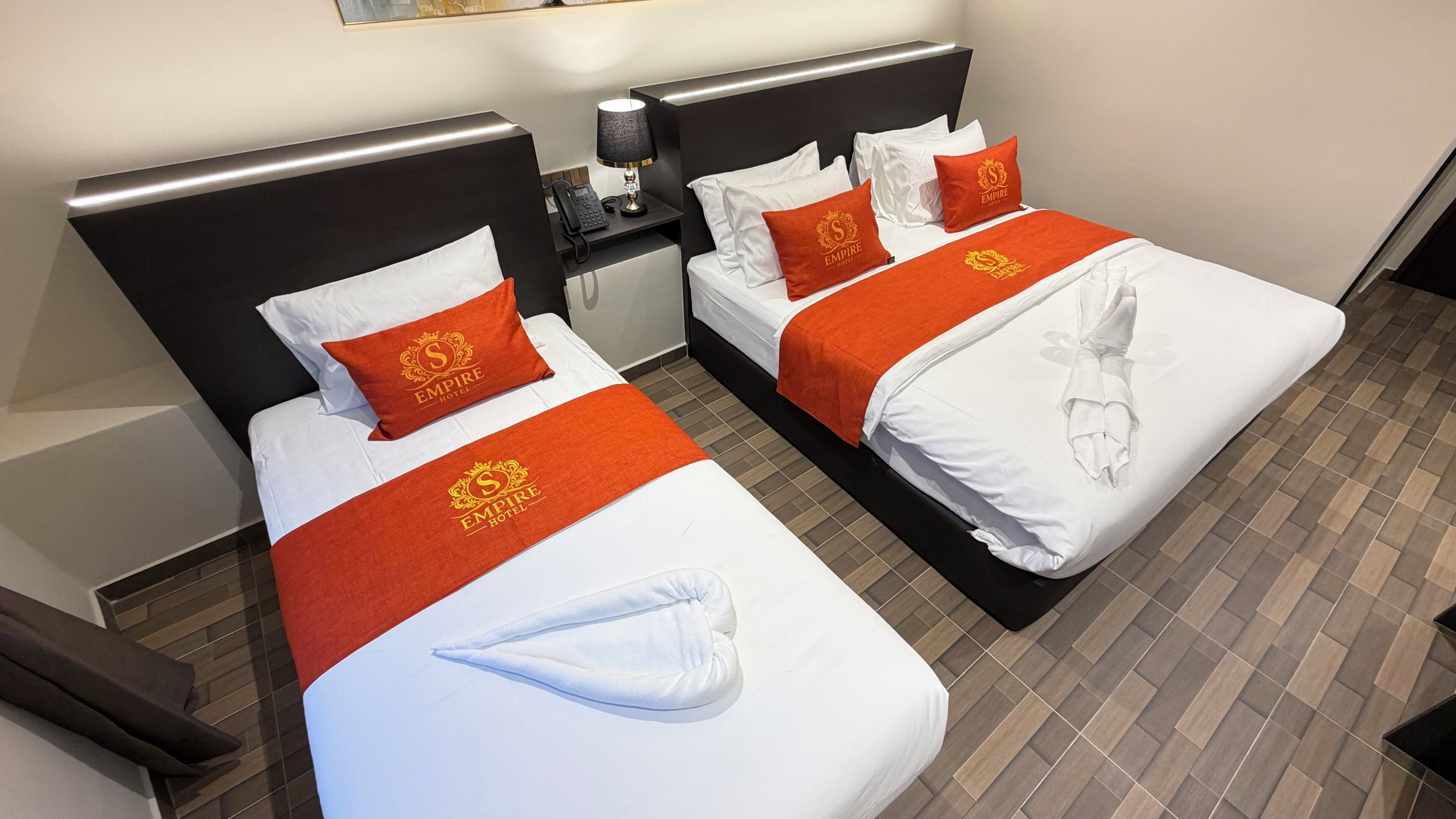A hotel room with two beds, each with white bedding and orange accents, including pillows and a blanket.