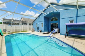 Piscina com águas cristalinas azuis, rodeada por área coberta com parede azul e estrutura de telhado.