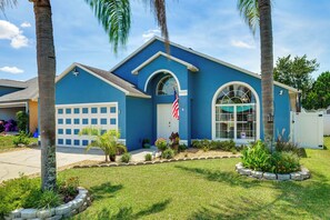 Uma casa residencial com fachada azul, garagem e um jardim frontal com plantas e uma bandeira.