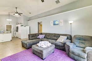 Uma sala de estar com um sofá seccional cinza, um banquinho do mesmo tom e um tapete roxo.
