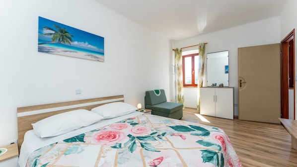 Una habitación de hotel con cama, una silla, un armario y un cuadro de una playa.