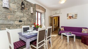 Una sala acogedora con una pared de piedra, una mesa de comedor para dos personas y un sofá morado.