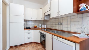 Una cocina con armarios blancos, encimera de madera, cafetera, hervidor y pileta.