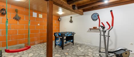 A room with a foosball table, exercise equipment, a swing set, and a brick wall.