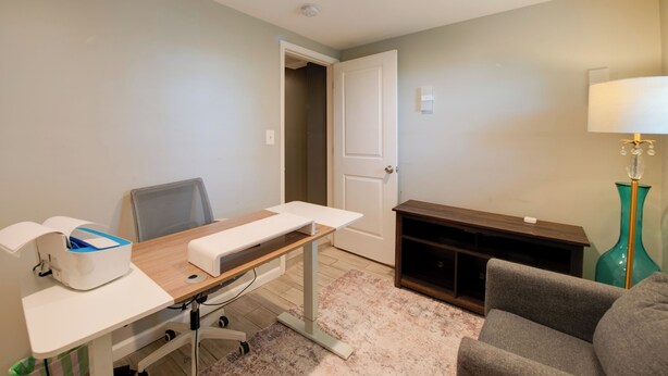 Una habitación con escritorio, silla y un pequeño sofá. Se ve una puerta que da a otra habitación.