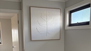Um corredor com corrimão de madeira, uma porta e uma obra de arte com folhas fixada na parede.