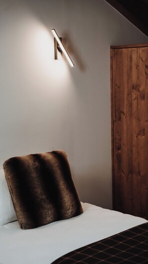 A bedroom with a bed, a wooden wardrobe, and a wall-mounted light fixture. - DOMA Chalet Le Tera (balcony, mountain views, and parking in Méribel) (Les Allues)