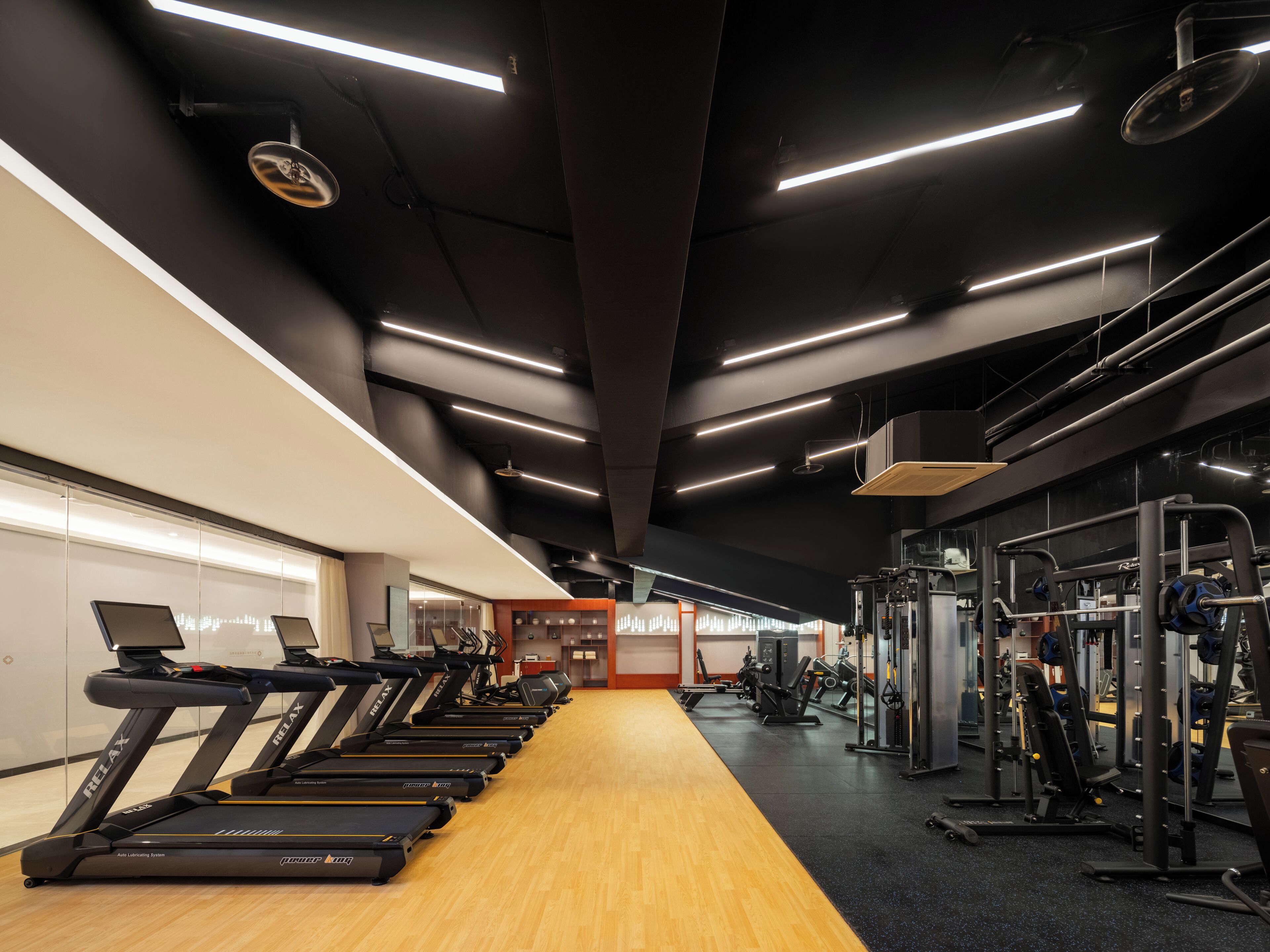 Uma academia com esteiras, máquinas de musculação e piso de madeira.