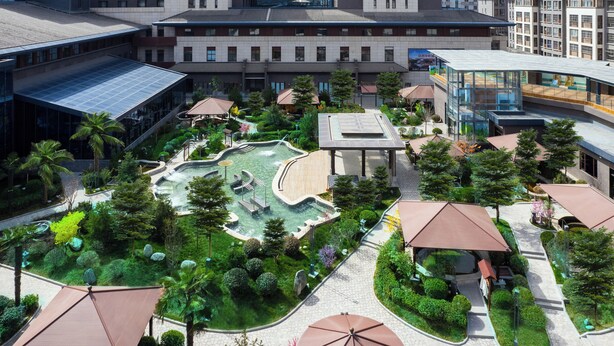 A modern building with a courtyard featuring a water feature, surrounded by greenery and covered seating areas. - LANDISON HUABIN HOT-SPRING HOTEL SHAANXI (Baoji)