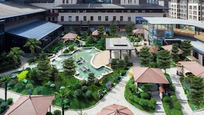 A modern building with a courtyard featuring a water feature, surrounded by greenery and covered seating areas.