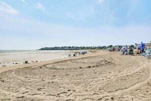 A beach with a sandy shore, beach chairs, umbrellas, and a row of houses in the background. - Tiny Antique Cottage - 2 Minutes From Short Sands! (York)