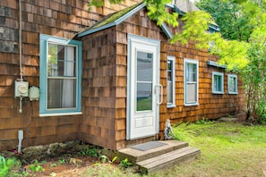 Una casa de madera con puerta principal, dos ventanas y un pequeño porche con escalones.