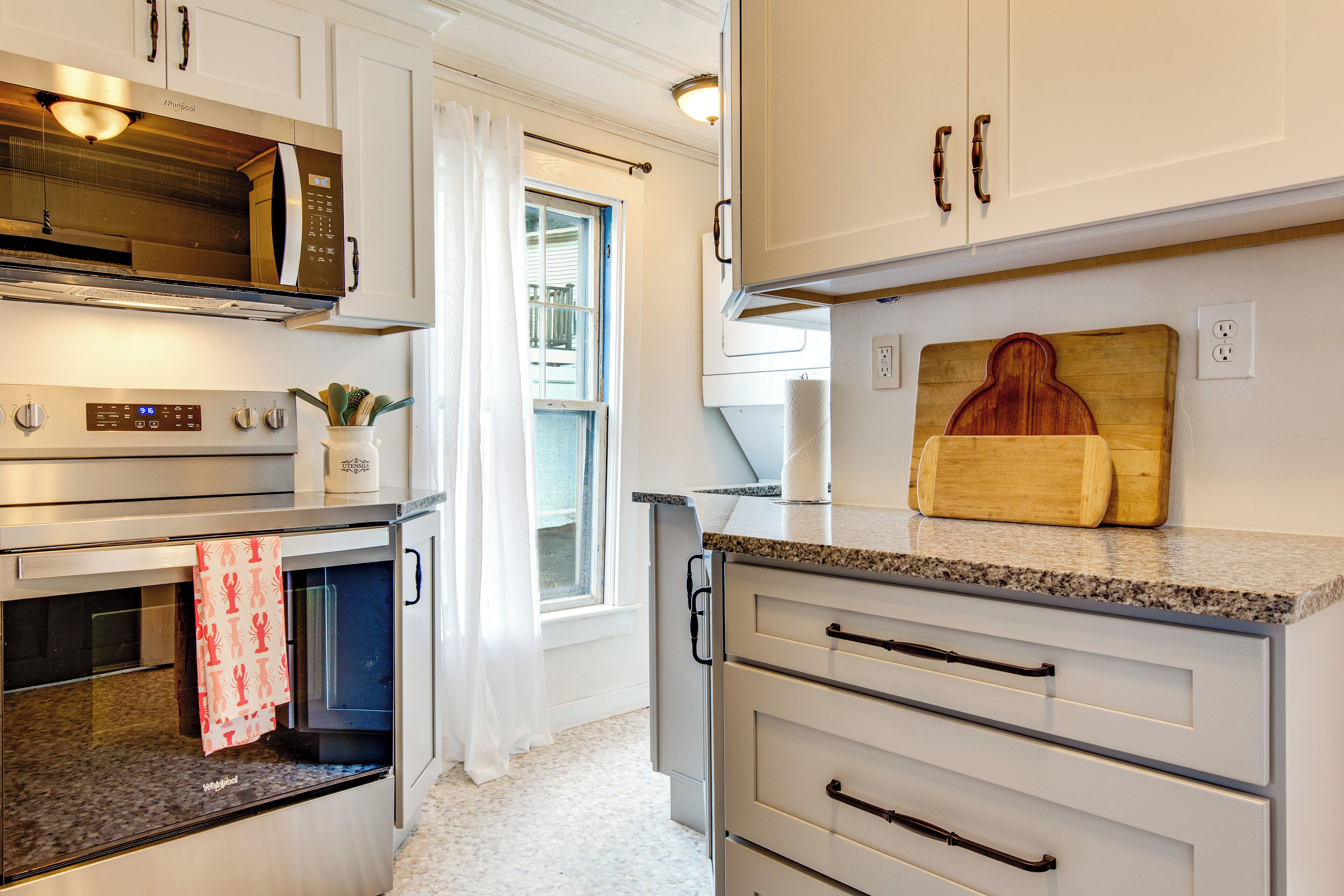 A modern kitchen with stainless steel appliances, a wooden cutting board, and a window with curtains.