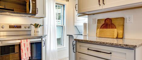 A modern kitchen with stainless steel appliances, a wooden cutting board, and a window with curtains.