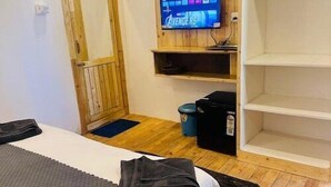 Une chambre avec un lit, un téléviseur fixé au mur, une armoire en bois et une petite étagère.